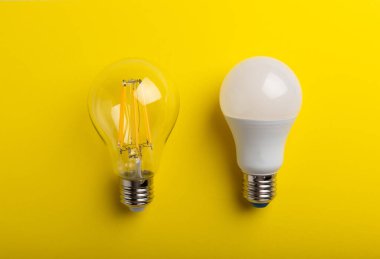 Elektrik ampulleri. Enerji verimliliği kavramı. LED lamba parlak lambaya karşı. Sarı arka planda kompozisyon. Ekonomik ve çevre dostu bir ampul kavramı kullan.