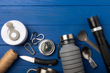 Set of tourist equipment on a blue wooden background.EDC set.flat lay.Camping plate,mug,bottle,spoon,flashlight and compass.Copy space.Top view.Travel concept.Set of tourist equipment