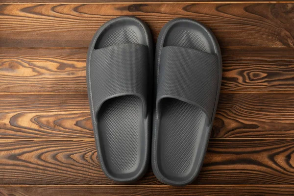 Kahverengi ahşap arka planda şık lastik terlikler. Değiştirilebilir plaj ayakkabıları. Uzayı kopyala. Metin için yer.