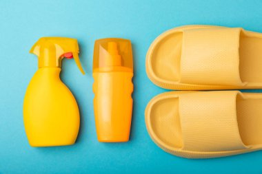 Mavi arka planda plaj aksesuarları olan düz bir kompozisyon. Plaj terlikleri ve güneş kremi. Güneş koruması. Kopyalamak için yer. Ders için yer..