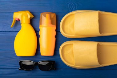 Düz kompozisyon ve mavi dokuya sahip plaj aksesuarları. Plaj terlikleri, güneş gözlüğü ve güneş kremi. Güneş koruması. Kopyalama için yer. Ders için yer..