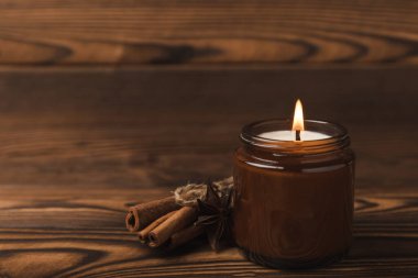 Kahverengi cam bir kavanozda yanan sıcak bir mum tarçın çubukları ve kahverengi ahşap dokusunda balkabağı mumları. Kışın ev dekorasyonu. Soya ekolojik mumu. 