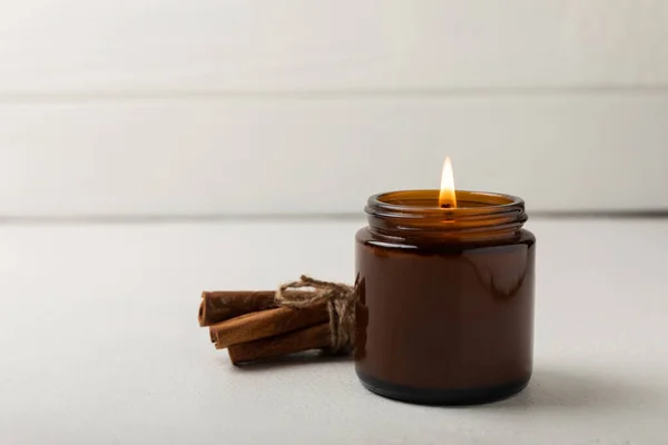 Cozy Burning Candle Brown Glass Jar Cinnamon Sticks White Wood — Foto Stock