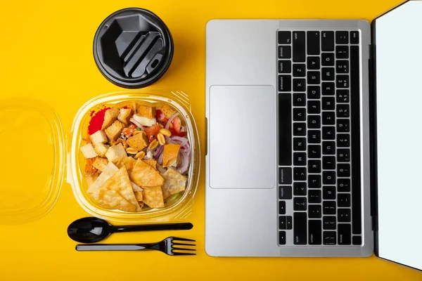 Office work, lunches and home delivery. Poke with seafood and funchose on a yellow background with a laptop and a blank screen. Food delivery concept.Japanese food.Copy space. Place for text.