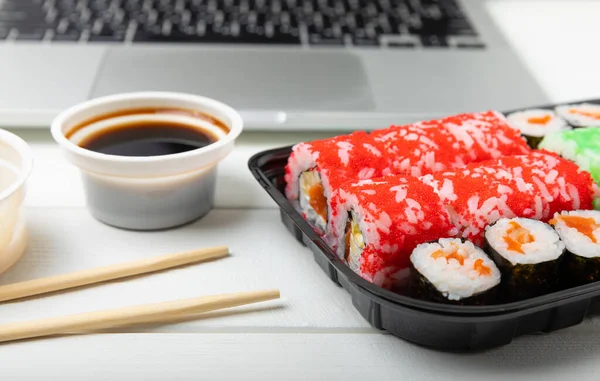 Office work, lunches and home delivery. Seafood sushi set on white table with laptop and blank screen. Food delivery concept.Japanese food.Copy space. Place for text.