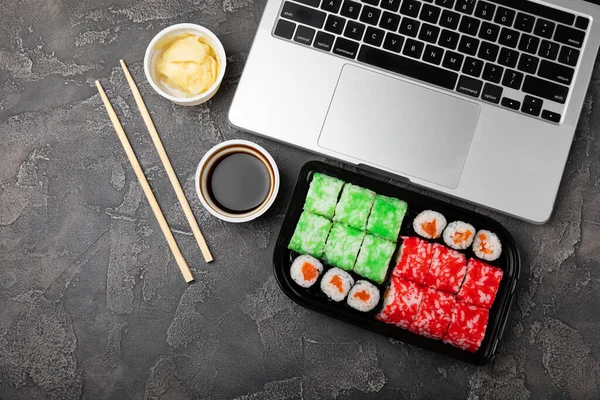 Office work, lunches and home delivery. Seafood sushi set on black table with laptop and blank screen. Food delivery concept.Japanese food.Copy space. Place for text.