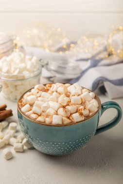 Bir fincan lezzetli kakao içeceği ve mavi bardakta şekerlemeler. Beyaz dokuma masasında kış içecekleri için şekerlemeler ve şekerlemeler. Kış sıcak içeceği. Şekerleme ve baharatlı sıcak çikolata..