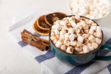 Bir fincan lezzetli kakao içeceği ve mavi bardakta şekerlemeler. Beyaz dokuma masasında kış içecekleri için şekerlemeler ve şekerlemeler. Kış sıcak içeceği. Şekerleme ve baharatlı sıcak çikolata..