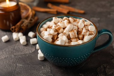 Bir fincan lezzetli kakao içeceği ve mavi bardakta şekerlemeler. Siyah dokuma masasında kış içecekleri için marşmelovlar ve şekerlemeler. Kış sıcak içeceği..