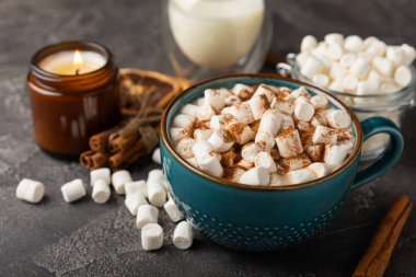 Bir fincan lezzetli kakao içeceği ve mavi bardakta şekerlemeler. Siyah dokuma masasında kış içecekleri için marşmelovlar ve şekerlemeler. Kış sıcak içeceği..