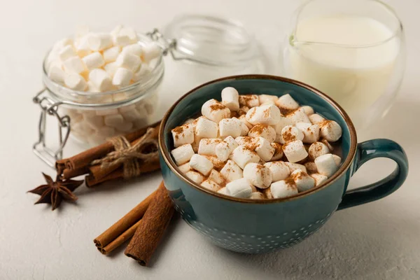 Bir fincan lezzetli kakao içeceği ve mavi bardakta şekerlemeler. Beyaz dokuma masasında kış içecekleri için şekerlemeler ve şekerlemeler. Kış sıcak içeceği. Şekerleme ve baharatlı sıcak çikolata..