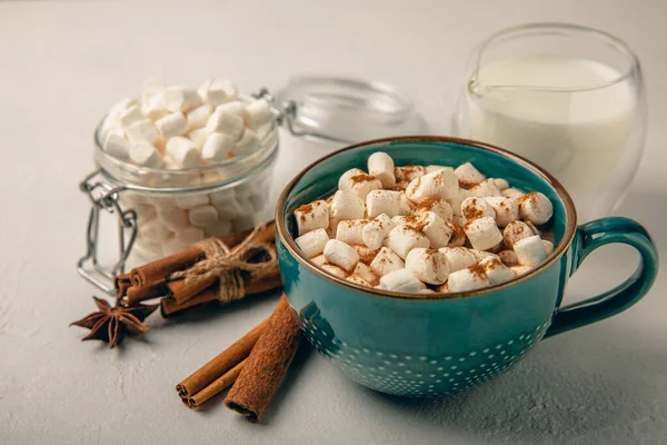 Bir fincan lezzetli kakao içeceği ve mavi bardakta şekerlemeler. Beyaz dokuma masasında kış içecekleri için şekerlemeler ve şekerlemeler. Kış sıcak içeceği. Şekerleme ve baharatlı sıcak çikolata..