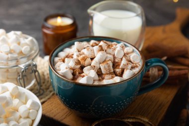 Bir fincan lezzetli kakao içeceği ve mavi bardakta şekerlemeler. Siyah dokuma masasında kış içecekleri için marşmelovlar ve şekerlemeler. Kış sıcak içeceği..