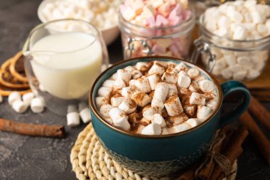 Bir fincan lezzetli kakao içeceği ve mavi bardakta şekerlemeler. Siyah dokuma masasında kış içecekleri için marşmelovlar ve şekerlemeler. Kış sıcak içeceği..