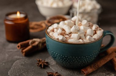 Bir fincan lezzetli kakao içeceği ve mavi bardakta şekerlemeler. Siyah dokuma masasında kış içecekleri için marşmelovlar ve şekerlemeler. Kış sıcak içeceği..