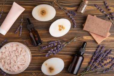 Lavender spa. Sea salt, lavender flowers, body scrub and cream and handmade soap. Natural herbal cosmetics with lavender flowers on brown texture background.