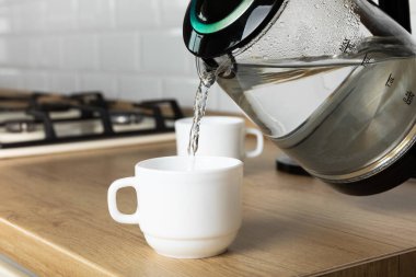 A man makes tea using boiling water from an electric kettle in the kitchen at home. It's time to have breakfast and drink tea. Modern electric kettle on a wooden table. Kettle for boiling water.