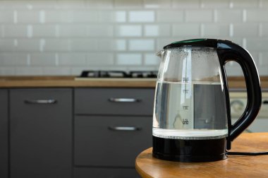 Modern electric transparent kettle on a wooden table in the kitchen.Kettle for boiling water and making tea.Home appliances for making hot drinks.Space for copy.Place for text.