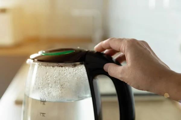 Close-up of a woman pressing the power switch on an electric kettle.Kettle for boiling water and making tea.Home appliances for making hot drinks.Space for copy.Place for text.