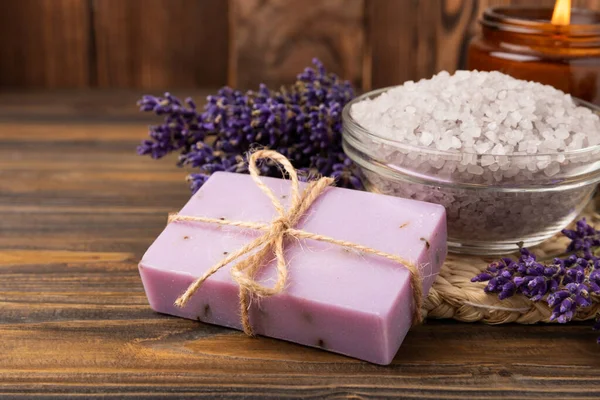 Lavender spa. Sea salt, lavender flowers, essential oils, body cream and handmade soap. Natural herbal cosmetics with lavender flowers on brown texture background. Relax and spa concept. Space for text.