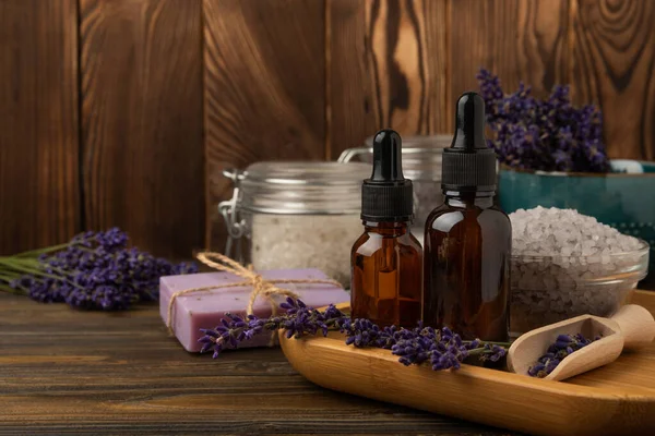 Lavender spa. Sea salt, lavender flowers, essential oils, body cream and handmade soap. Natural herbal cosmetics with lavender flowers on brown texture background. Relax and spa concept. Space for text.