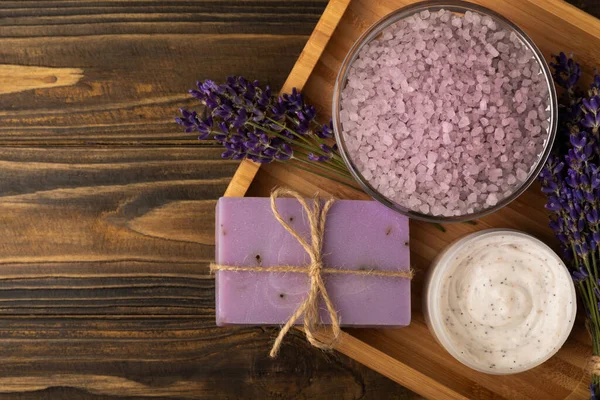 Lavender spa. Sea salt, lavender flowers, essential oils, body cream and handmade soap. Natural herbal cosmetics with lavender flowers on brown texture background. Relax and spa concept. Space for text.