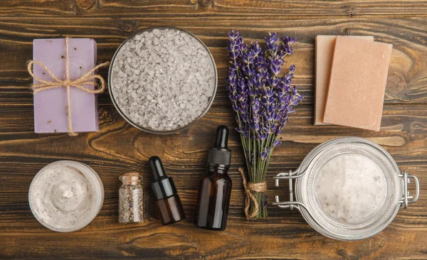 Lavender spa. Sea salt, lavender flowers, essential oils, body cream and handmade soap. Natural herbal cosmetics with lavender flowers on brown texture background. Relax and spa concept. Space for text.