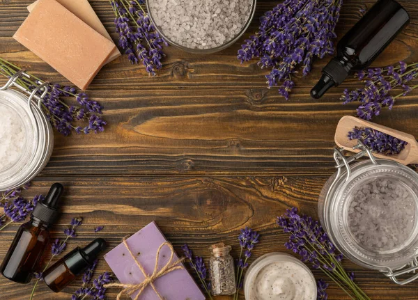 Lavender spa. Sea salt, lavender flowers, essential oils, body cream and handmade soap. Natural herbal cosmetics with lavender flowers on brown texture background. Relax and spa concept. Space for text.
