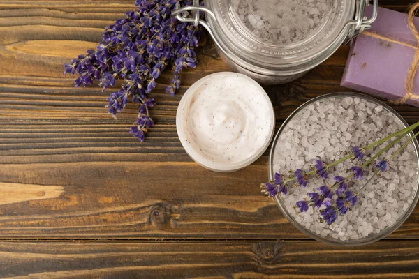 Lavender spa. Sea salt, lavender flowers, essential oils, body cream and handmade soap. Natural herbal cosmetics with lavender flowers on brown texture background. Relax and spa concept. Space for text.