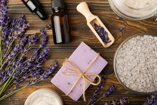 Lavender spa. Sea salt, lavender flowers, essential oils, body cream and handmade soap. Natural herbal cosmetics with lavender flowers on brown texture background. Relax and spa concept. Space for text.