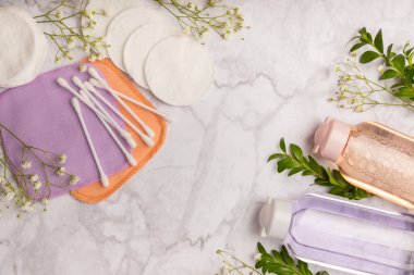 Micellar water, makeup remover wipes, cotton swabs and flowers. Cleansing the skin of sebum and makeup. Composition on a white marble background. Beauty concept. Copy space text. flat lay