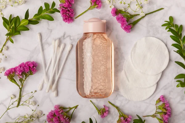 Micellar water, makeup remover wipes, cotton swabs and flowers. Cleansing the skin of sebum and makeup. Composition on a white marble background. Beauty concept. Copy space text. flat lay