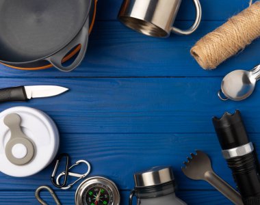 Set of tourist equipment on a blue background. EDC set flat lay. Camping plate, mug, bottle, knife, rope, spoon and compass.