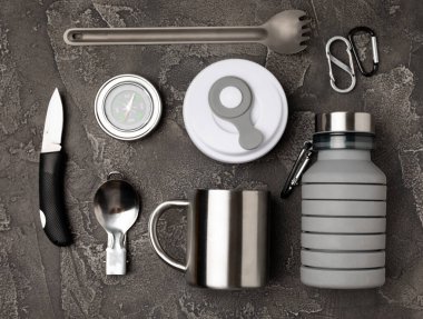 Set of tourist equipment on a black background. EDC set flat lay. Camping plate, mug, bottle, knife, rope, spoon and compass.