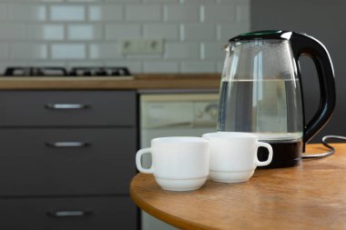 Modern electric transparent kettle with tea cups on a wooden table in the kitchen. Kettle for boiling water and making tea. Household appliances for making hot drinks. Place to copy. Place for text.