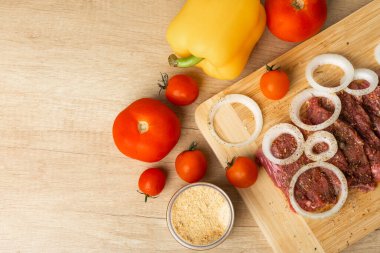 Raw beef with onions marinated with spices and vegetables on a light texture background.Recipe for cooking meat.Juicy steak on a bamboo board, close-up. Place for text, space for copy.