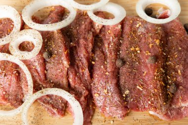 Raw beef with onions marinated with spices on light texture background.Meat cooking recipe.Juicy steak on a bamboo board, close-up. Place for text, space for copy.