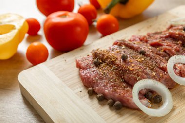 Raw beef with onions marinated with spices and vegetables on a light texture background.Recipe for cooking meat.Juicy steak on a bamboo board, close-up. Place for text, space for copy.