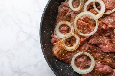 Raw beef with onions marinated with spices in a frying pan on a light texture background.Recipe for cooking meat. Place for text, space for copy.