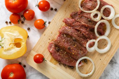 Raw beef with onions marinated with spices and vegetables on a light texture background.Recipe for cooking meat.Juicy steak on a bamboo board, close-up. Place for text, space for copy.
