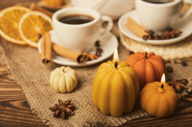 Candles in the form of pumpkins with fragrant coffee on a background of spicy spices of star anise and cinnamon on a brown wooden background.Cozy home decor.Halloween concept.Happy Thanksgiving.