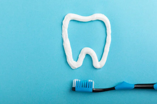 Oral care. Dental care. Composition with a toothbrush and a figure of a tooth with toothpaste on a blue background. Teeth love concept.Copy space. Place for text.Fletley