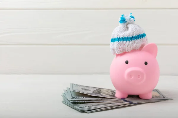 Savings concept. Piggy bank and money on white texture wood.Piggy bank in a warm winter hat,saving heat. Saving heating concept.Place for text. Copy space