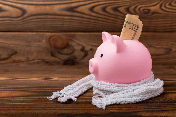 Savings concept. Piggy bank and money on a brown wooden table.Piggy bank in a warm scarf, heat saving. Saving heating concept.Place for text. Copy space