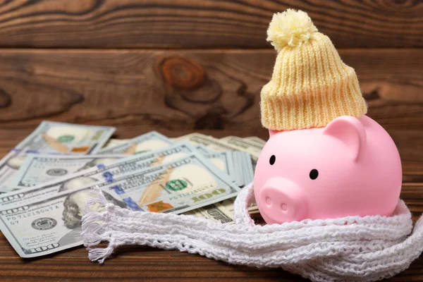 Savings concept. Piggy bank and money on a brown wooden table. Piggy bank in a warm winter hat and scarf, heat saving. Saving heating concept.Place for text. Copy space