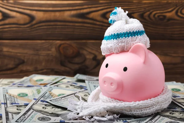 Savings concept. Piggy bank and money on a brown wooden table. Piggy bank in a warm winter hat and scarf, heat saving. Saving heating concept.Place for text. Copy space