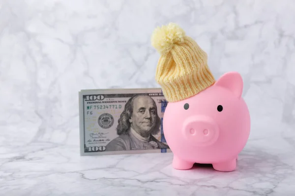 Savings concept. Piggy bank and money on a marble table.Piggy bank in a warm winter hat,saving heat. Saving heating concept.Place for text. Copy space