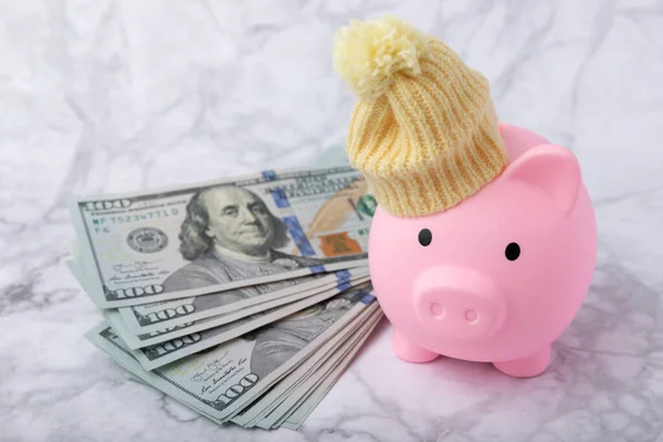 Savings concept. Piggy bank and money on a marble table.Piggy bank in a warm winter hat,saving heat. Saving heating concept.Place for text. Copy space