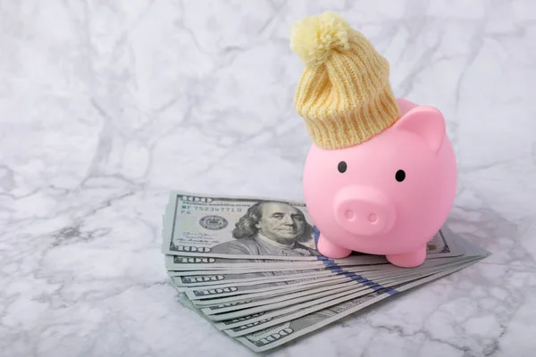 Piggy bank with money.Piggy bank with dollars in winter hat and scarf on white marble.Heat saving concept. The concept of saving heating.Banking and savings. Place for text, space for copy.