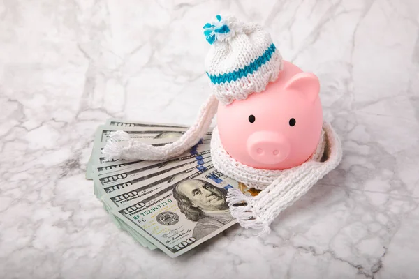 Piggy bank with money.Piggy bank with dollars in winter hat and scarf on white marble.Heat saving concept. The concept of saving heating.Banking and savings. Place for text, space for copy.